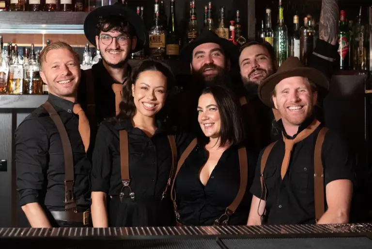 Spiritual Parlor team photo in uniform, featuring staff in black dress shirts and natural brown leather suspenders, St. George, UT cocktail bar with live music.